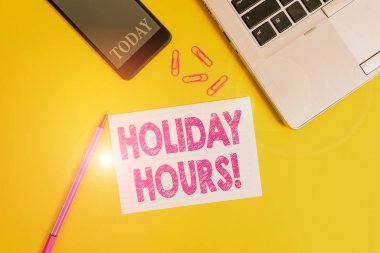 Sözcük yazarlığı, Holiday Hours. Esnek çalışma saatleri altında çalışanlar için fazla mesai konsepti Moda açık dizüstü bilgisayar akıllı telefon işaretleyici kağıt ataçları renkli arka plan.
