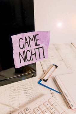 Game Night 'ı gösteren bir not yazıyorum. İş fotoğrafı gösterimi genellikle arkadaşlarıyla poker gibi yetişkin oyun tarihlerinde yapılır. Klavye ve durağanlık yakınlarındaki siyah bilgisayar ekranına yapıştırılmış not kağıdı..