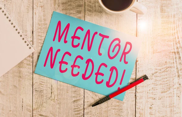 Text sign showing Mentor Needed. Conceptual photo Employee training under senior assigned act as advisor Stationary placed next to a cup of black coffee above the wooden table.