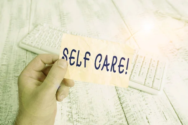 Text sign showing Self Care. Conceptual photo practice of taking action to preserve or improve ones own health man holding colorful reminder square shaped paper white keyboard wood floor. — Stock Photo, Image