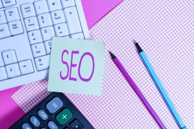 Seo 'yu gösteren bir not yazıyorum. İş fotoğraflarının çok etkili bir şekilde satışa sunulması. Yakın işyerinizin internet üzerinden satışa çıkarılması için. Not kağıdı renkli hediye paketinin yanındaki klavyeye yapışmış..