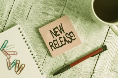 Yeni Sürüm 'ü gösteren not yazılıyor. İş fotoğrafı sergisi, son zamanlarda haber değeri taşıyan bir şeyi duyuruyor. Ahşap masanın üzerinde bir fincan sade kahvenin yanına koyulmuş..