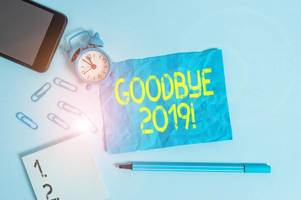 Text sign showing Goodbye 2019. Conceptual photo express good wishes when parting or at the end of last year Alarm clock clips notepad smartphone sheet marker colored background.