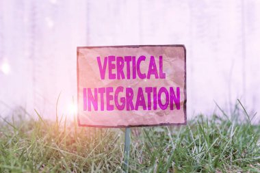 Dikey Bütünleşme için el yazısı metni. Kavram, üretimin farklı aşamalarındaki şirketlerin birleşmesi anlamına geliyor. Kırışık kağıtlar bir çubuğa bağlanıp yeşil çimenli topraklara yerleştirildi..