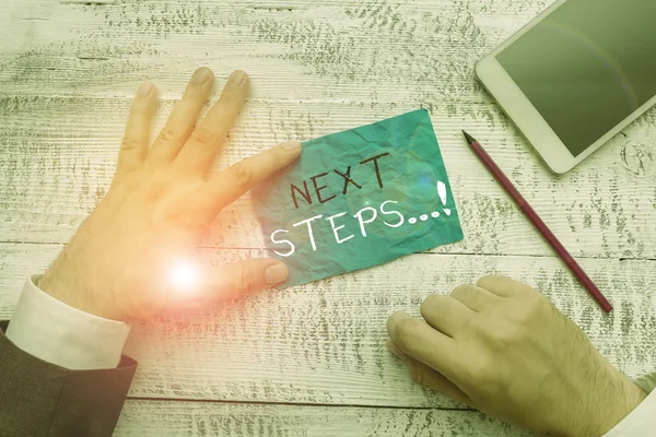 Schrijfbriefje met volgende stappen. Zakelijke foto presentatie van iets wat je doet nadat je klaar bent met het doen van de eerste een Hand note papier in de buurt van het schrijven van apparatuur en smartphone. — Stockfoto