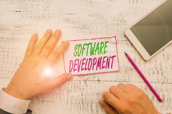 Conceptual hand writing showing Software Development. Business photo showcasing software is created using a specific programming Hand hold note paper near writing equipment and smartphone.