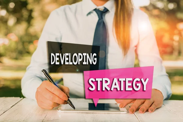 Handwriting text Developing Strategy. Concept meaning Game plan that sets specific goals and objectives Female business person sitting by table and holding mobile phone. — Stock Photo, Image