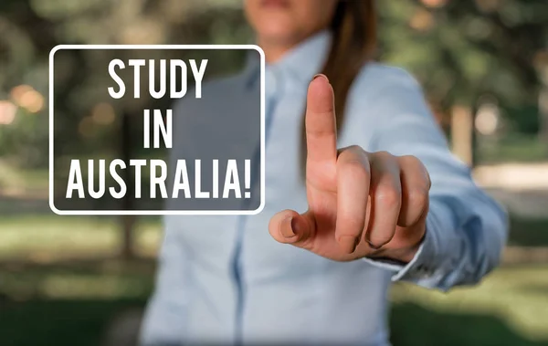 Handwriting text writing Study In Australia. Concept meaning going into foreign country order complete your studies Woman in a blue business shirts pointing with her finger into empty space.