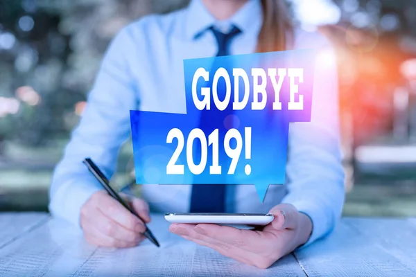 Текст для написання слів Godbye 2019. Бізнес-концепція для вираження добрих побажань при розлученні або в кінці минулого року Жіночий бізнесмен сидить за столом і тримає мобільний телефон . — стокове фото