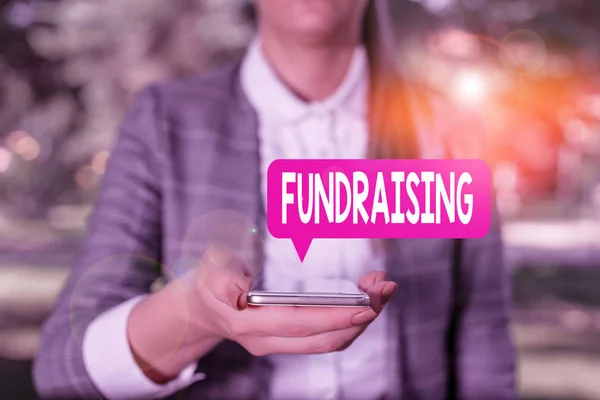 Writing note showing Fundraising. Business photo showcasing act of collecting or producing money for a particular purpose Woman in grey suites holds mobile phone.