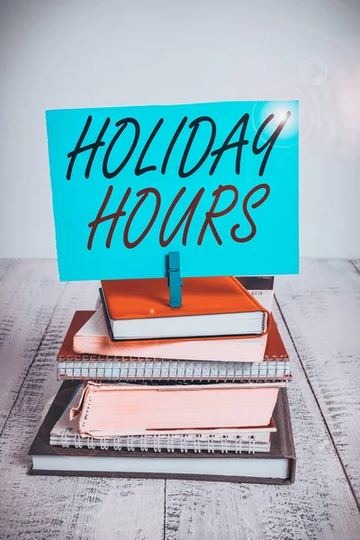 Handwriting text writing Holiday Hours. Concept meaning employee receives twice their normal pay for all hours pile stacked books notebook pin clothespin colored reminder white wooden.