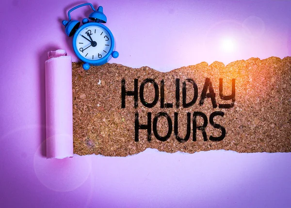 Text sign showing Holiday Hours. Conceptual photo employee receives twice their normal pay for all hours Alarm clock and torn cardboard placed above a wooden classic table backdrop. — Stock Photo, Image