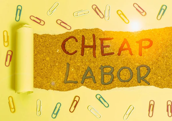 Handwriting text Cheap Labor. Concept meaning when a demonstrating works hard in bad conditions and very little money Paper clip and torn cardboard placed above a wooden classic table backdrop.