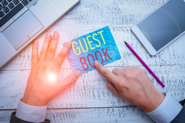 Conceptual hand writing showing Guest Book. Business photo text electronic means for a visitor to acknowledge a visit to a site Hand hold note paper near writing equipment and smartphone.