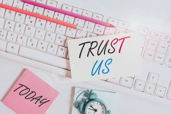 Text sign showing Trust Us. Business photo showcasing to believe that someone is good and honest and will not harm Flat lay above empty note paper on the pc keyboard pencils and clock