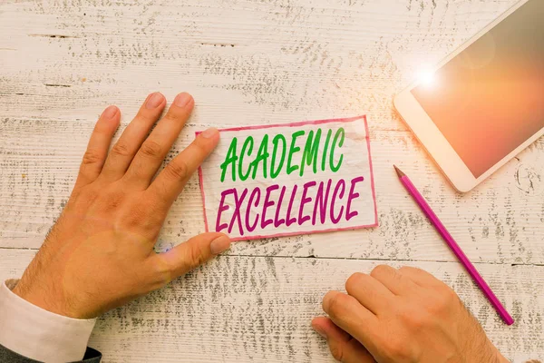 Conceptual hand writing showing Academic Excellence. Concept meaning Achieving high grades and superior perforanalysisce Hand hold note paper near writing equipment and smartphone