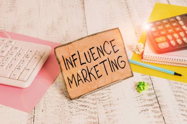 Text sign showing Influence Marketing. Business photo showcasing Using key leaders to drive a brand s is message to market Notepaper stand on buffer wire in between computer keyboard and math sheets