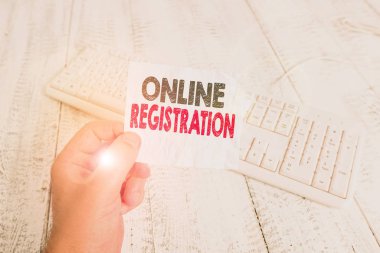 Online Kayıt 'ı gösteren bir not yazıyorum. İnternet üzerinden ürünün kullanıcısı olarak kaydolmak için iş kavramı. Elinde renkli hatırlatıcı kare şeklindeki kağıt ahşap zemin tutan bir adam.