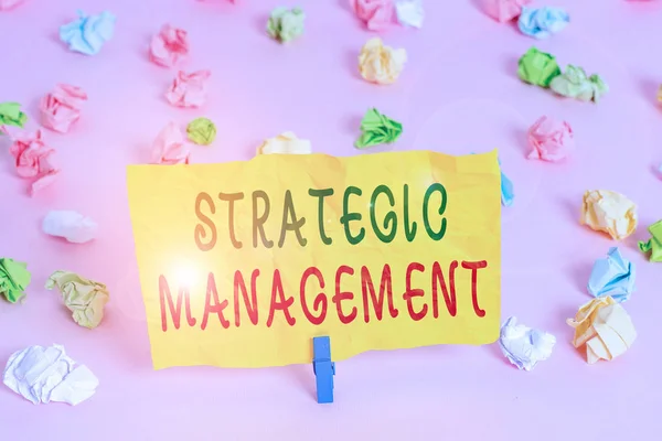 Handwriting text writing Strategic Management. Conceptual photo formulation and implementation of the major goals Colored crumpled papers empty reminder pink floor background clothespin