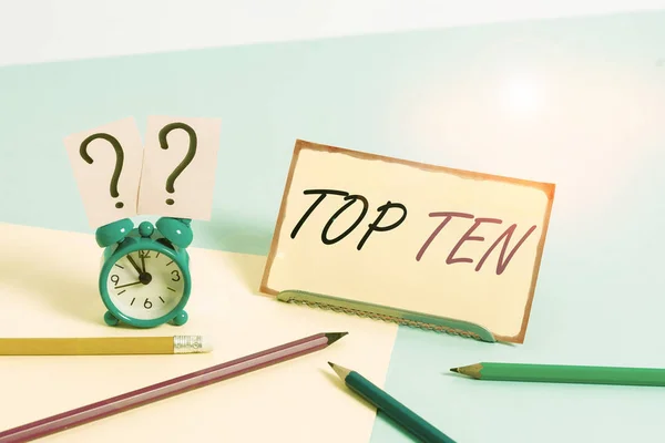 Handwriting text Top Ten. Conceptual photo the ten most popular songs or recordings in the popular music charts Mini size alarm clock beside stationary placed tilted on pastel backdrop
