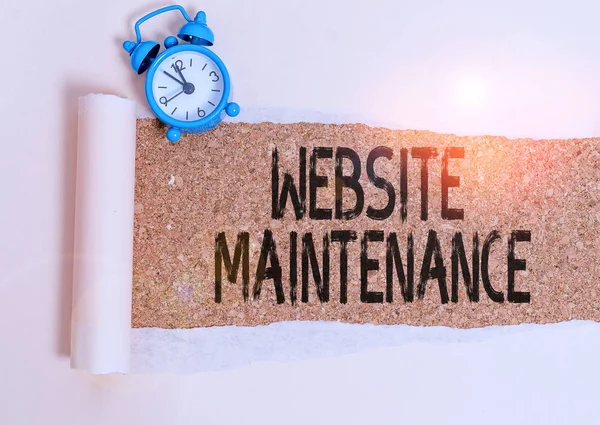 Writing note showing Website Maintenance. Business concept for act of regularly checking your website for issues Alarm clock and torn cardboard on a wooden classic table backdrop