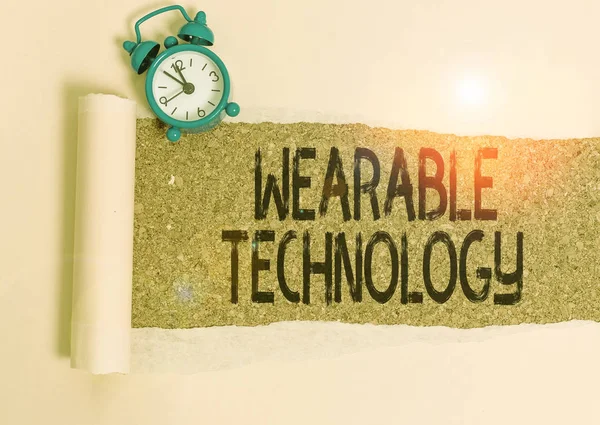 Writing note showing Wearable Technology. Business concept for electronic devices that can be worn as accessories Alarm clock and torn cardboard on a wooden classic table backdrop