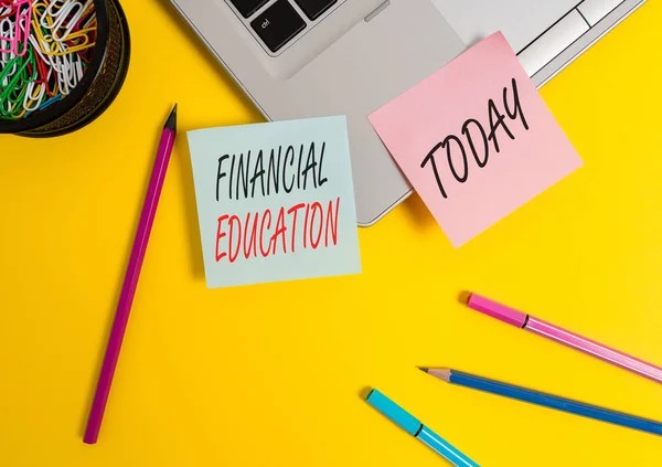 Conceptual hand writing showing Financial Education. Concept meaning education and understanding of various financial areas Laptop sticky notes container pencils markers colored background