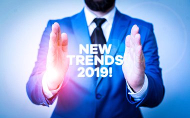 Kelime yazma metni Yeni Eğilimler 2019. İş fotoğraflarında genel bir yön gösteriliyor. Masanın önünde elleri açık bir şekilde gelişmekte olan bir adam. Cep telefonu ve notlar masanın üzerinde.