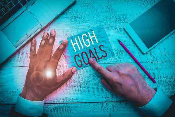 Conceptual hand writing showing High Goals. Concept meaning object of a demonstrating s is ambition or effort An aim or desired result Hand hold note paper near writing equipment and smartphone