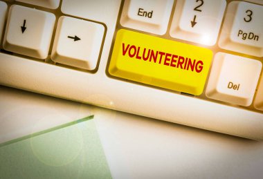 Gönüllü olduğunu gösteren bir not yazıyorum. Finansal kazanç sağlamayan hizmetleri sağlamak için iş konsepti beyaz arkaplanının üzerinde not kağıdı olan beyaz pc klavye zorunluluğu