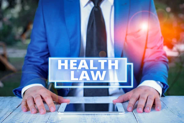 Writing note showing Health Law. Business concept for law to provide legal guidelines for the provision of healthcare Businessman in blue suite with a tie holds lap top in hands