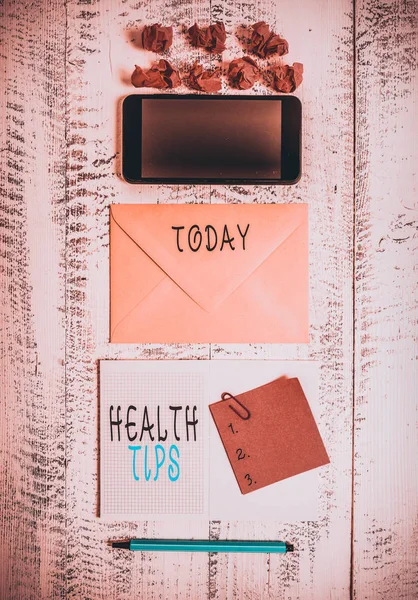 Handwriting text writing Health Tips. Conceptual photo advice or information given to be helpful in being healthy Envelop smartphone notepad note clip marker paper balls wooden background