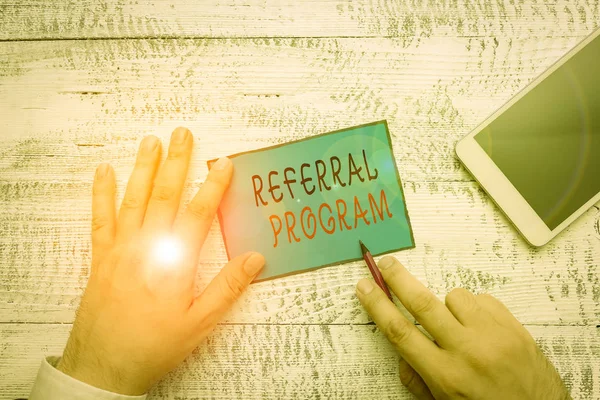 Conceptual hand writing showing Referral Program. Concept meaning employees are rewarded for introducing suitable recruits Hand hold note paper near writing equipment and smartphone