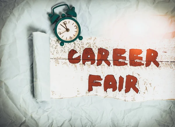 Conceptual hand writing showing Career Fair. Concept meaning an event at which job seekers can meet possible employers Alarm clock and torn cardboard on a wooden classic table backdrop