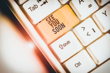 See You Soon 'u gösteren bir not yazıyorum. Biriyle vedalaşmak için kullanılan iş konsepti ve yakında tekrar buluşacak beyaz arka planda nota kağıdıyla birlikte White Pc klavyesi