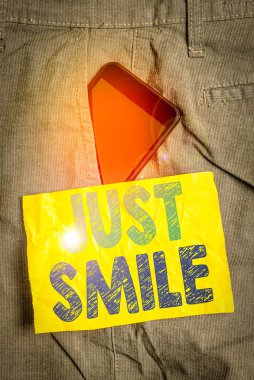 Just Smile 'ı gösteren bir not yazıyorum. İş konsepti, pantolonun içinde zevk ya da eğlence amaçlı bir telefon cihazını gösteren bir yüz ifadesi varsayımı ön cepli kağıt.
