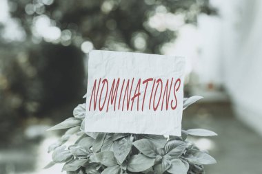 Conceptual hand writing showing Nominations. Concept meaning action of nominating or state being nominated for prize Plain paper attached to stick and placed in the grassy land clipart