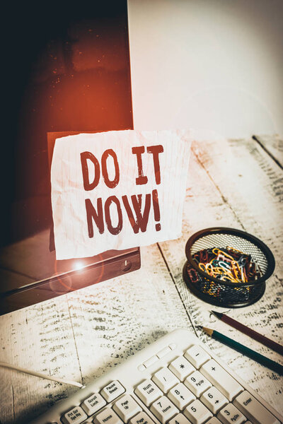 Text sign showing Do It Now. Business photo showcasing not hesitate and start working or doing stuff right away Note paper taped to black computer screen near keyboard and stationary
