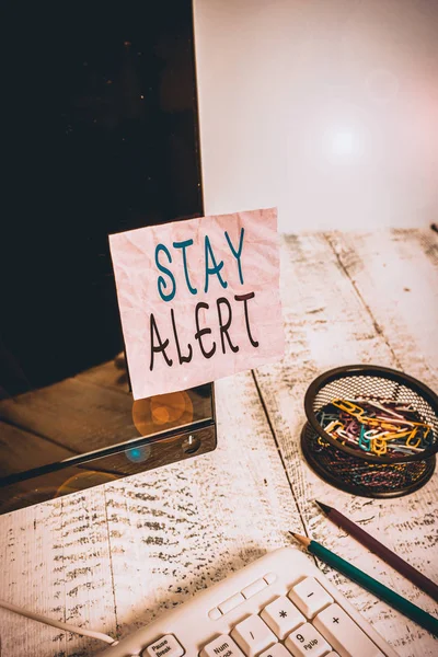 Handwriting text writing Stay Alert. Conceptual photo Paying full attention to things around Quick to see or understand Note paper taped to black computer screen near keyboard and stationary