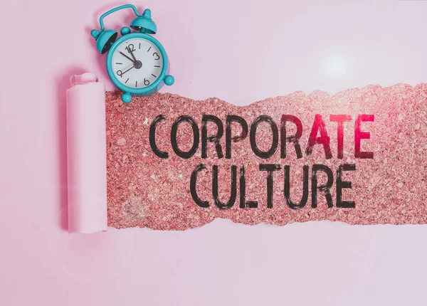 Text sign showing Corporate Culture. Business photo showcasing pervasive values and attitudes that characterize a company Alarm clock and torn cardboard placed above a wooden classic table backdrop