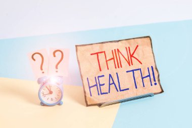 Think Health 'i gösteren bir not yazıyorum. Fiziksel ve sosyal refahın tam durumu için iş kavramı Pastel zemin üzerine yerleştirilmiş kağıdın yanında alarmlı saat