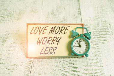 Love More Worry less 'ı gösteren bir not yazıyorum. İyi bir davranış motivasyonu için iş konsepti Sevimli yaşam için Alarm saati not kağıdının önünde eğildi