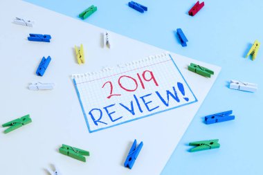 2019 Review 'ı gösteren bir not yazıyorum. Geçen yılki olayları hatırlamak için iş konsepti ana eylemler veya iyi gösteriler Sarı mavi arkaplan ile renkli çamaşır iğnesi kağıt hatırlatıcısı
