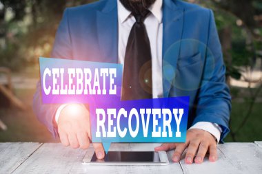 Kelime yazma metni İyileşmeyi Kutla. Yaralı ya da acı çeken herkes için fotoğraf toplama programı. Mavi süitteki kravatlı iş adamı dizüstü bilgisayarı elinde tutuyor.