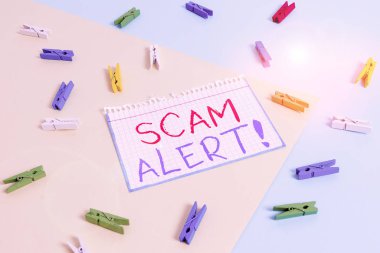 Scam Alert 'i gösteren not yazılıyor. Dolandırıcılık konsepti, kurbandan para kazanmak için onu sarı mavi arka planlı renkli çamaşır iğnesi kâğıdı hatırlatıcısıyla ikna etmek.