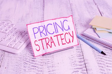 Fiyat Stratejisini gösteren bir not yazıyorum. Şirketlerin ürünlerini veya hizmetlerini fiyatlandırmak için kullandıkları iş konsepti. Bilgisayar klavyesi ve sayfaları arasında tel üzerine not defteri.