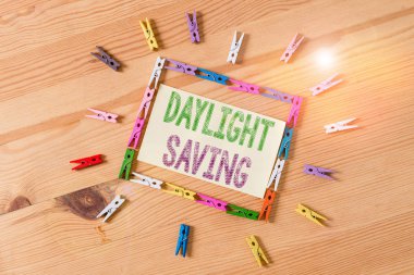 Kelime yazma metni Daylight Tasarruf. İş fotoğrafı gösterimi, sıcak hava yaklaştıkça saati öne alıyor. Renkli çamaşır iğnesi kağıtları boş ahşap zemin ofisini hatırlatıyor.
