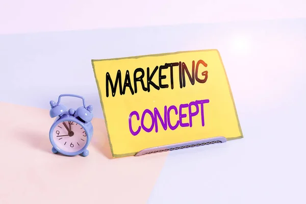 Text sign showing Marketing Concept. Business photo showcasing the strategy that firms adopt to satisfy customers Mini size alarm clock beside a Paper sheet placed tilted on pastel backdrop