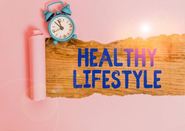 Kelime yazma metni Sağlıklı Yaşam Tarzı. Ciddi şekilde hasta olma riskini azaltan iş fotoğrafı gösterme şekli. Alarm saati ve yırtılmış karton kutu klasik masa arkaplanının üzerine yerleştirilmiş.