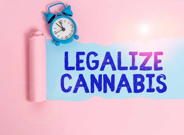 大麻の合法化を示すメモを書く 合法化されたレクリエーション大麻が全国的に使用する法律のためのビジネスコンセプトアラームクロックとプレーンパステルテーブルの背景の上に置かれた引き裂かれた段ボール — ストック写真